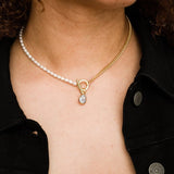 A person wearing the Larissa Loden Fonda Half Chain Pearl Necklace—featuring freshwater pearls, a gold chain, toggle clasp, and small pendant—over a black denim jacket. This hypoallergenic piece adds modern elegance to any outfit.