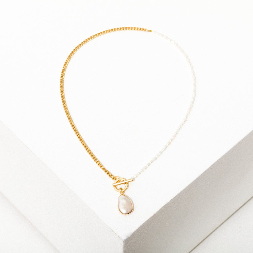 The Fonda Half Chain Pearl Necklace by Larissa Loden features a gold plated half chain, half freshwater pearls, and a single oval pearl pendant, beautifully displayed on a white surface.