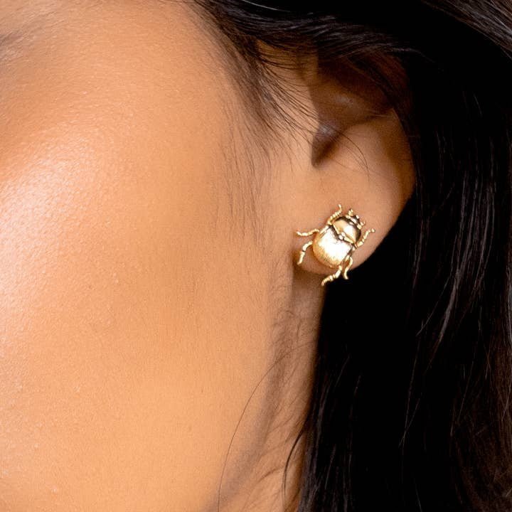 A close-up of a person wearing Peter and June’s Fortune Beetle Studs—18K gold plated beetle-shaped earrings.