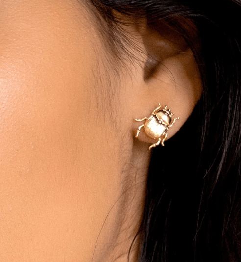 Close-up of a person's ear wearing the Fortune Beetle Studs by Peter and June, 18k gold plated and beetle-shaped.