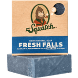 A box of Dr.Squatch Bar Soap in Fresh Falls stands behind an unboxed blue bar, featuring "Alaskan Glacier Mineral Clay" and "Zero Grit" on its packaging, for a clean, refreshing shower experience.