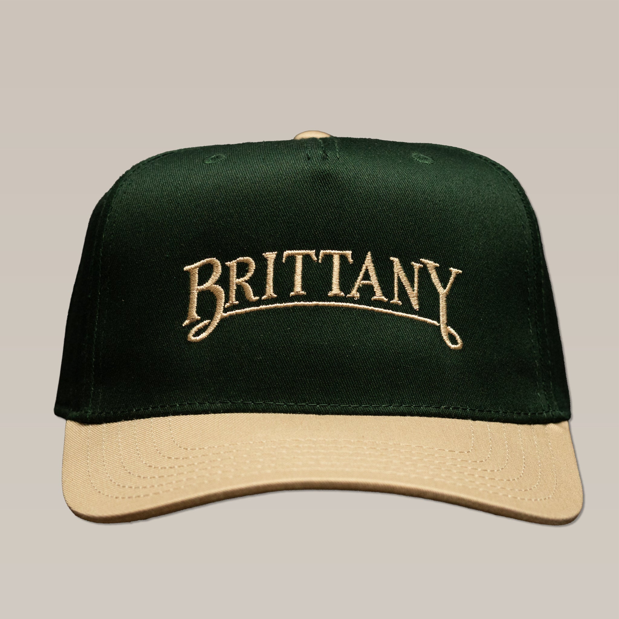 A dark green Bird Dog Series Hat | Brittany with a tan brim and “BRITTANY” embroidered in tan, perfect as a durable hunting companion.