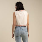 A woman stands with her back to the camera, wearing the Frontier Vest by Sendero Provisions Co.—a sleeveless, cream-colored embroidered floral vest—paired with light blue jeans, set against a plain beige background.