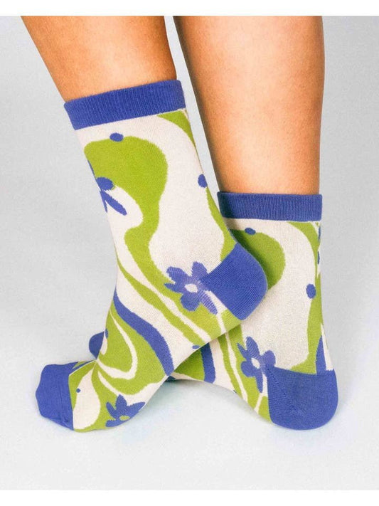 Two feet wear Funky Squiggly Flowers Knit Ankle Socks by Hannah Packer for Tailored Union, showing a 70's-inspired green, blue, and white abstract floral pattern with bold blue cuffs, heels, and toes.