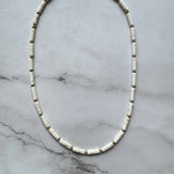 The Gabriela Necklace by Jessica Matrasko Jewelry showcases cylindrical white beads with gold spacers, arranged in an oval shape against a light marble background.