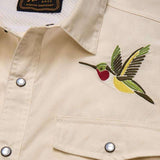 The Howler Brothers Gaucho Snapshirt | Nectar Seekers features a beige design with embroidered hummingbird art above the left chest pocket and a visible brand label inside the collar—a fresh update to the classic western shirt.