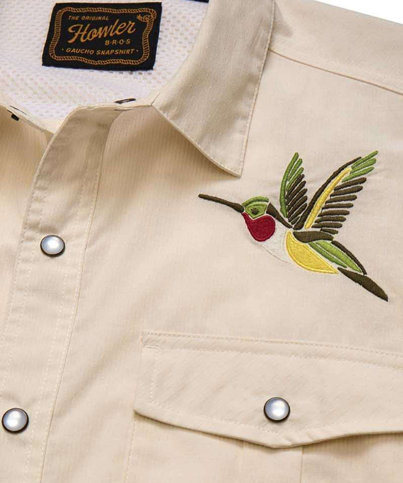 The Howler Brothers Gaucho Snapshirt | Nectar Seekers features a beige design with embroidered hummingbird art above the left chest pocket and a visible brand label inside the collar—a fresh update to the classic western shirt.