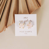 A pair of hypoallergenic Gemstone Prong - Rose Quartz - Gold Earrings by JaxKelly is shown on a card labeled "JaxKelly, wear good vibes, rose quartz, love" against a neutral background.