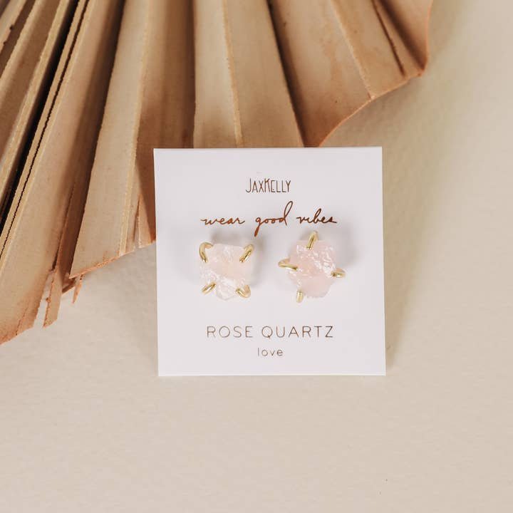 A pair of hypoallergenic Gemstone Prong - Rose Quartz - Gold Earrings by JaxKelly is shown on a card labeled "JaxKelly, wear good vibes, rose quartz, love" against a neutral background.