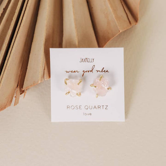 Gemstone Prong - Rose Quartz - Gold Earrings by JaxKelly, featuring hypoallergenic studs with gold prongs, are displayed on a branded card against a neutral background with a dried palm leaf.