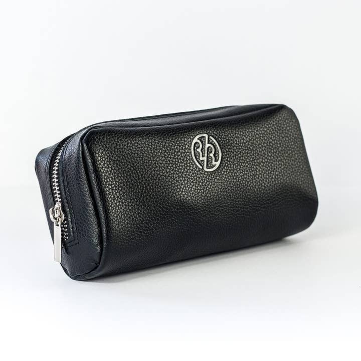 The Genuine Leather Dopp Kit by Rockwell Razors features black textured leather and a silver monogram logo, ideal for organizing grooming essentials. Photographed on a plain white background.