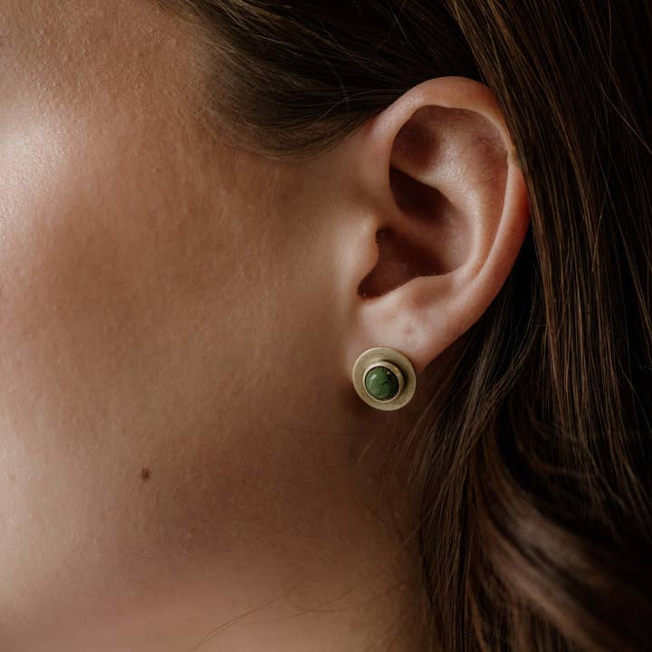 Close-up of a person’s ear wearing the Gibbon Studs by CommonForm—round sterling silver earrings featuring a turquoise stone set in a metal bezel.