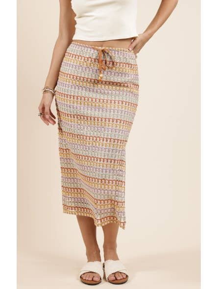 A person wearing a cream crop top, the Gilded Sky Midi Skirt by Sadie And Sage, bracelets, and white slide sandals stands against a neutral background.