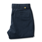 A pair of neatly folded navy blue Duck Head Gold School Chino pants with belt loops, a single back welt pocket, and a small yellow tag above the pocket.
