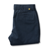 A neatly folded pair of Duck Head Gold School Chino pants in dark blue cotton twill with belt loops, a back pocket, and a small yellow tag near the waistband.