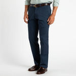 A man in Duck Head's Gold School Chino pants, a brown belt, brown dress shoes, and a light green button-up shirt stands against a white background.
