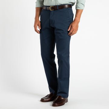 A man in a green checkered shirt, Duck Head Gold School Chino pants, a brown belt, and brown dress shoes stands against a plain white background.