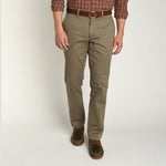 A man wears Duck Head Gold School Chino pants, a brown belt, brown shoes, and a plaid shirt while standing against a plain white background.
