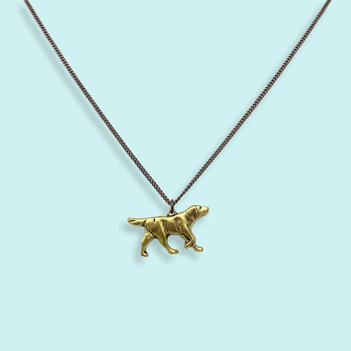 The Good Dog Necklace by Ornamental Things features a charming dog pendant on an aged brass chain, shown against a light blue background.