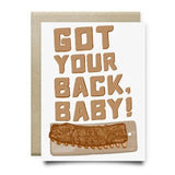 The "Got your back baby" A2 greeting card by Anvil Cards features bold brown text above a hand-drawn rack of ribs on a cutting board, all printed on sustainable linen paper.
