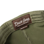 Close-up of the Duck Camp Grandpa Hat | Bass, an olive green polyester cap with a brown "Duck Camp Premium Outdoor Goods 100% Polyester" label, adjustable snapback, and detailed embroidered bass design.