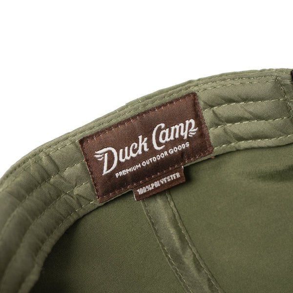 Close-up of the Duck Camp Grandpa Hat | Bass, an olive green polyester cap with a brown "Duck Camp Premium Outdoor Goods 100% Polyester" label, adjustable snapback, and detailed embroidered bass design.