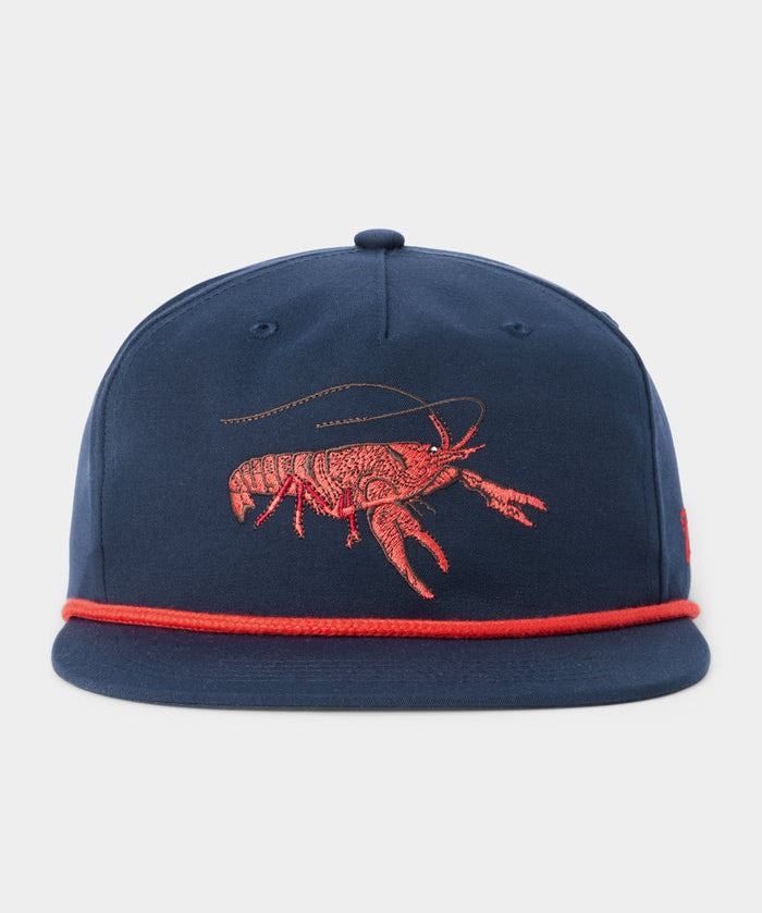 The Duck Camp Grandpa Hat Crawfish is a navy blue cap featuring an embroidered red crawfish, red rope detail above the brim, and an adjustable snapback closure for the perfect fit.