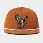 The Grandpa Hat | Dove by Duck Camp is a brown snapback cap with white trim and an embroidered bird with outstretched wings, inspired by dove poppers. Features an adjustable fit.