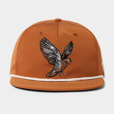 The Grandpa Hat | Dove by Duck Camp is a brown snapback cap with white trim and an embroidered bird with outstretched wings, inspired by dove poppers. Features an adjustable fit.