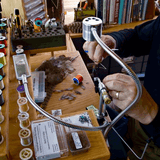 At a wooden workbench, someone arranges spools of thread, tools, feathers, and fly-tying materials to craft trout flies for their Guide Curated Fly Set by Mollyjogger.