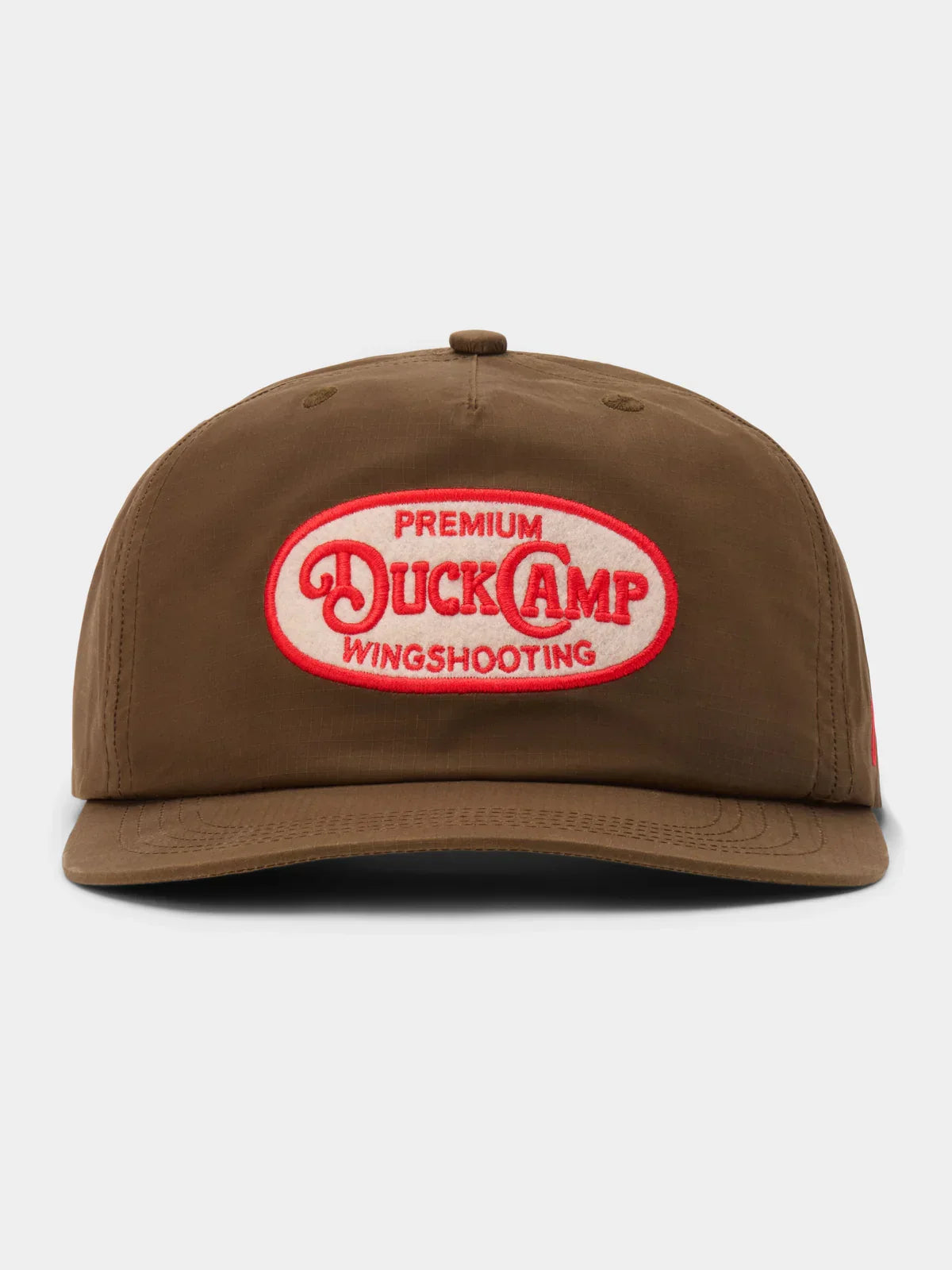 The Duck Camp Gunnison Wingshooting Badge Waxed Hat is a brown snapback cap with a red and white embroidered patch, crafted from durable, water-resistant waxed canvas—ideal for outdoor adventures.