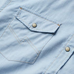 Close-up of the Howler Brothers H Bar B Snapshirt in Faded Blue Oxford, featuring a buttoned chest pocket, visible stitching, and signature pearl snaps.