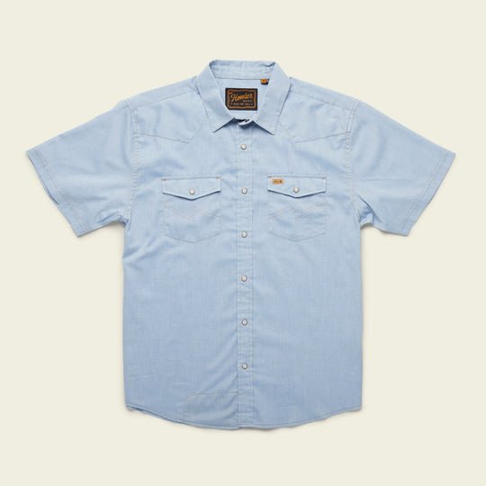The H Bar B Snapshirt by Howler Brothers in Faded Blue Oxford features short sleeves, pearl snaps, two chest pockets, and a collar, shown against a plain background.