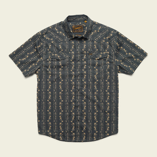 The H Bar B Snapshirt Hibiscus Ribbons by Howler Brothers is a relaxed fit short-sleeve shirt with a dark blue base, light floral vertical stripes, pearl snaps, and two flap chest pockets.