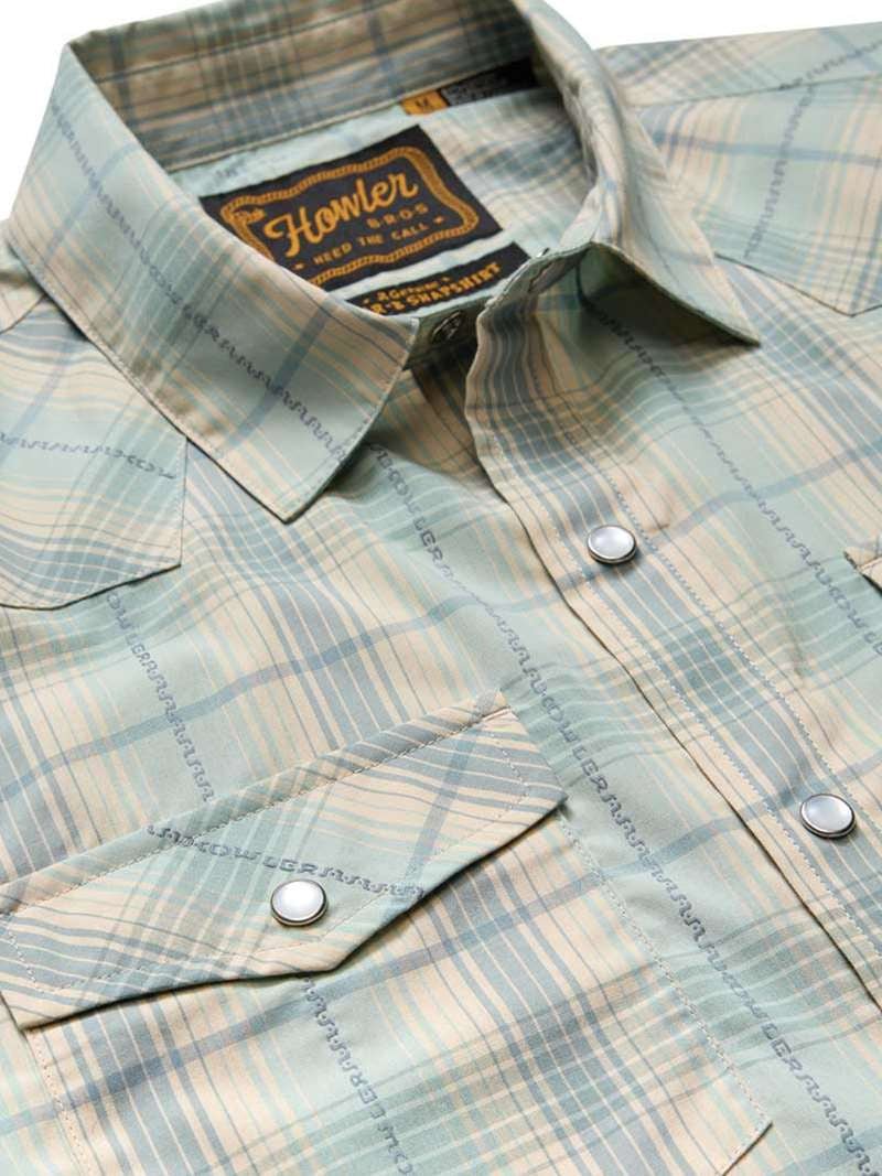 The H Bar B Snapshirt by Howler Brothers features a light green and beige plaid, pearl snaps, two front pockets, and "Howler Bros" branding on the inside collar tag.