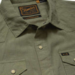Close-up of the olive green H Bar B Snapshirt by Howler Brothers, featuring pearl snaps, two chest pockets, and a visible brand label on the inside collar.