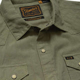 Close-up of the olive green H Bar B Snapshirt by Howler Brothers, featuring pearl snaps, two chest pockets, and a visible brand label on the inside collar.