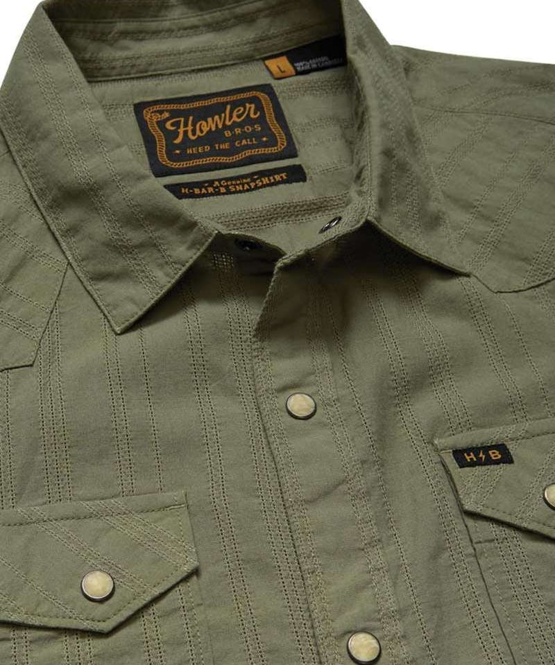 Close-up of the olive green H Bar B Snapshirt by Howler Brothers, featuring pearl snaps, two chest pockets, and a visible brand label on the inside collar.