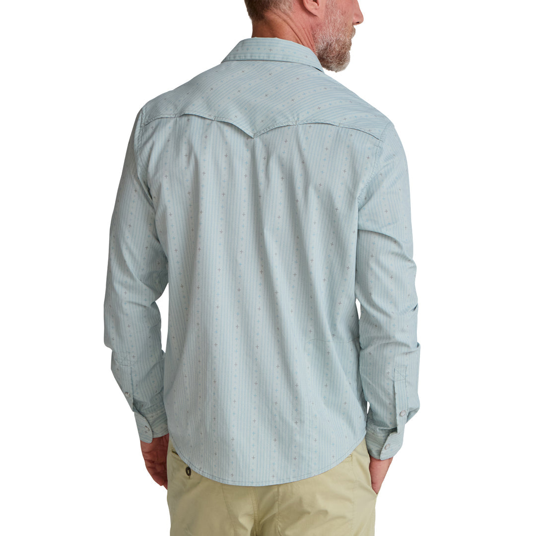 A man is shown from the back, looking to the side, wearing a light blue Howler Brothers H Bar B Tech Long Sleeve shirt and beige pants.