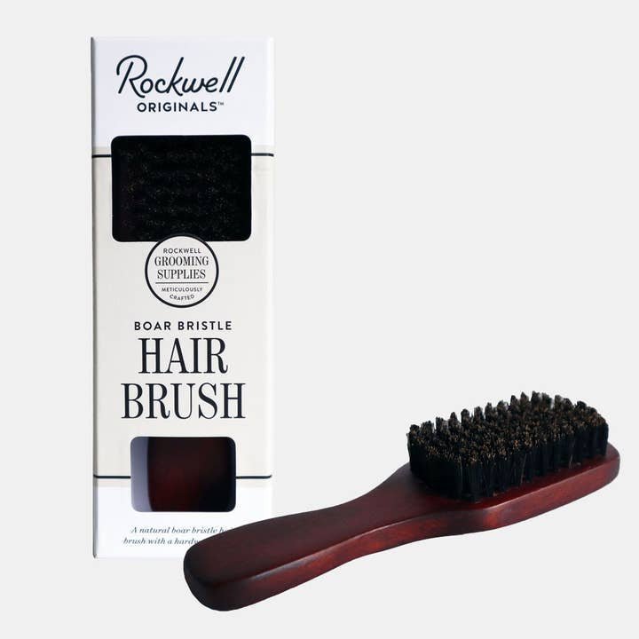 A Hair Brush by Rockwell Razors with natural bristles and a dark wooden handle is displayed beside its packaging box against a plain background.