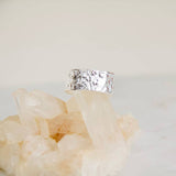 The Hammered Cuff Adjustable Ring by Mesa Blue, a textured hypoallergenic silver piece, is displayed atop translucent quartz crystals against a plain background.