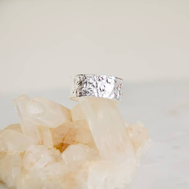 The Hammered Cuff Adjustable Ring by Mesa Blue, a textured hypoallergenic silver piece, is displayed atop translucent quartz crystals against a plain background.