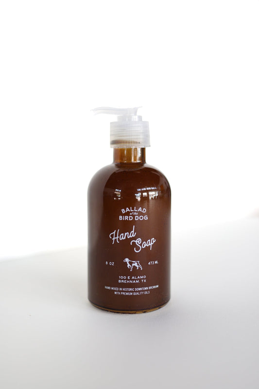 A brown bottle of Hand Soap | Ballad of the Bird Dog by Ballad of the Bird Dog, crafted with essential oils, features a white pump and sits on a white surface against a clean white background.