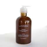 A brown pump bottle of Ballad of the Bird Dog Hand Soap with white text showing directions, Santal essential oil ingredients, and warnings stands on a white surface against a bright background.