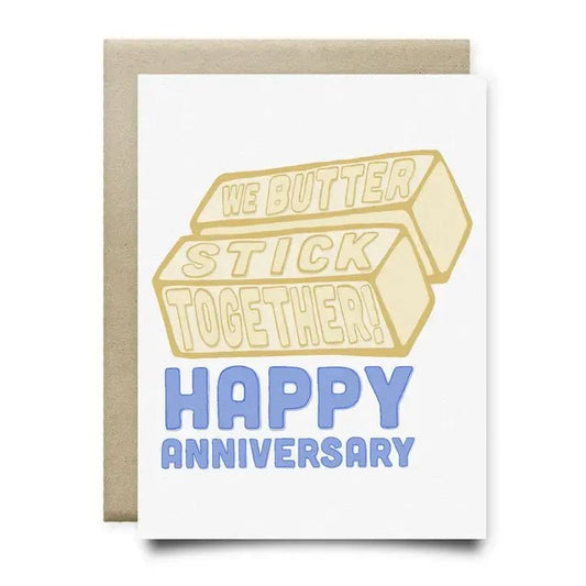 Anvil Cards' "Happy Anniversary" A2 greeting card features a hand-drawn design of two butter sticks with "We butter stick together!" above "Happy Anniversary" in blue, paired with a brown envelope and printed on sustainable linen paper.
