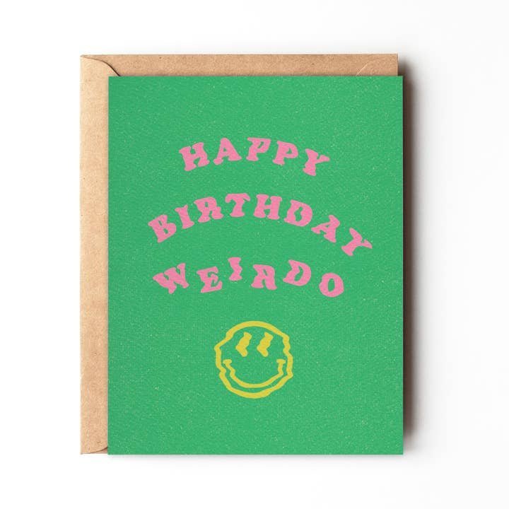The "Happy Birthday Weirdo" card by Daydream Prints features pink text and a yellow smiley face on green, comes with a brown envelope, and is a fun, eco-friendly greeting card option.