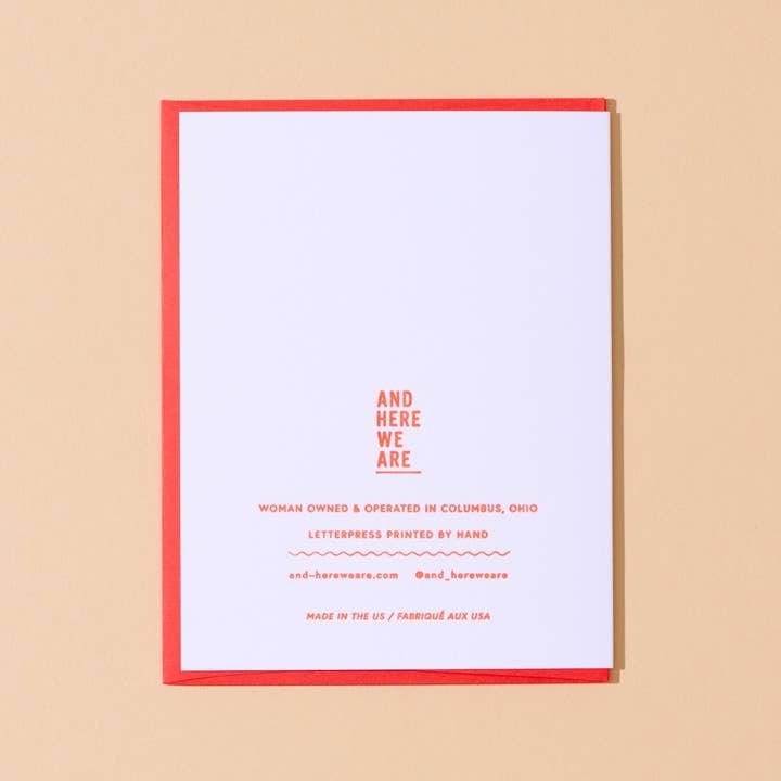The Happy Valentines Day Card by And Here We Are features vintage lettering, a red border, and is hand letterpress printed. It highlights the woman-owned Columbus, Ohio business with contact info and “And Here We Are” at the top.