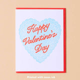 The Happy Valentines Day Card by And Here We Are features a blue lace heart, vintage “Happy Valentine’s Day” text, neon ink, a red border, and light beige background.