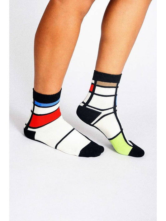 A person wearing Haus Socks Knit Ankle Socks by Tailored Union, featuring a mismatched geometric design inspired by Mondrian in red, blue, yellow, black, and white.