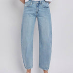 A person wearing Vervet High Rise Light Wash Barrel Leg Jeans with a white t-shirt and white flat shoes stands against a plain background.